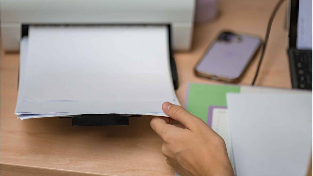 Person flipping through financial documents on a desk with a smartphone nearby.