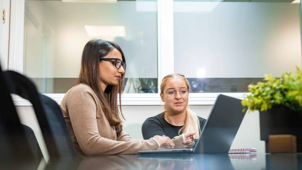 Two women discussing payroll at a desk with a laptop and documents.