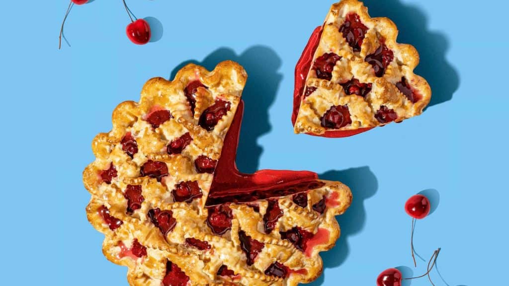 Cherry pie with a slice removed on a blue background.