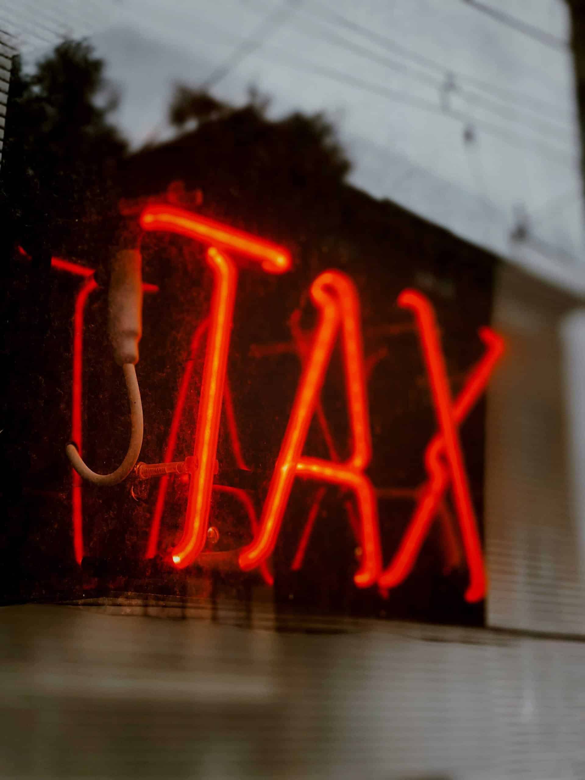 Neon 'TAX' sign in red glow outside a building.