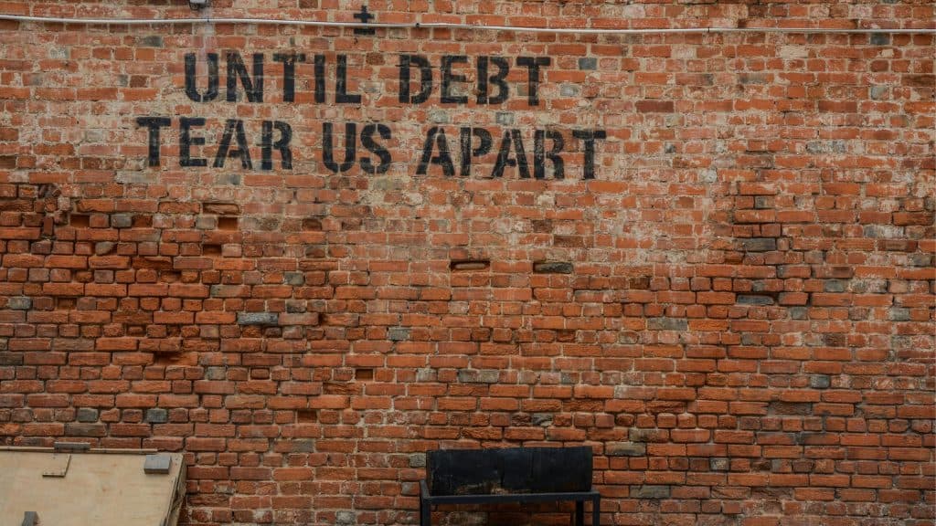 Graffiti on brick wall reading 'Until debt tear us apart'.