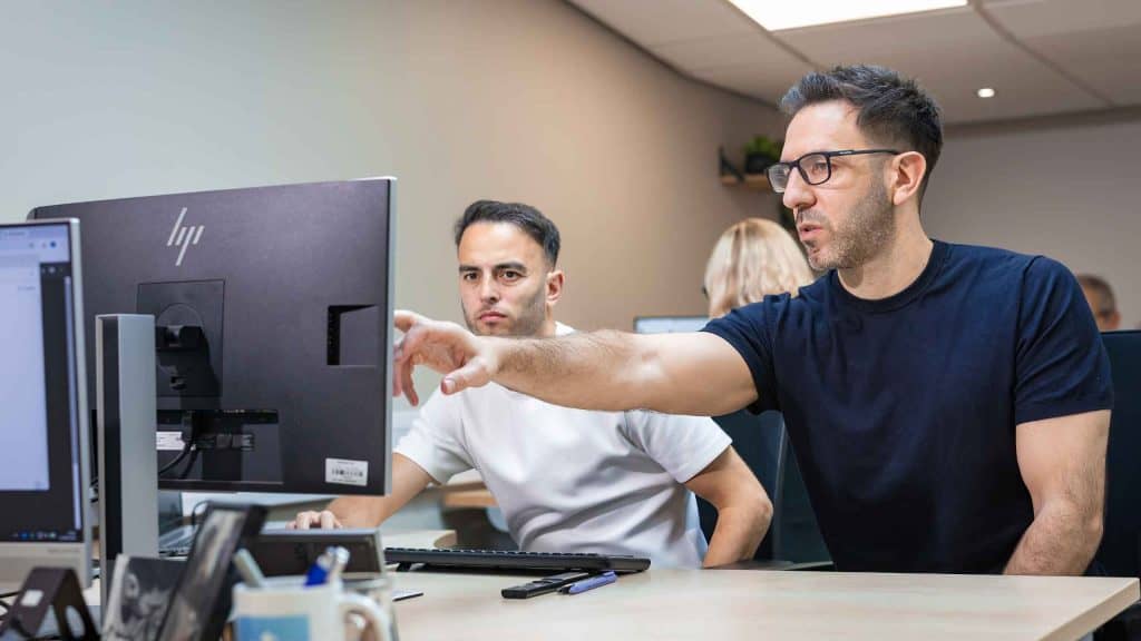 Two men discussing financial data in an office setting with computers.