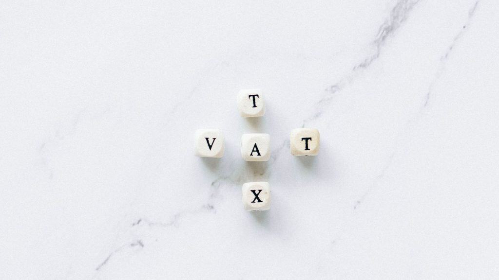 Wooden blocks spelling VAT on a white marble surface.