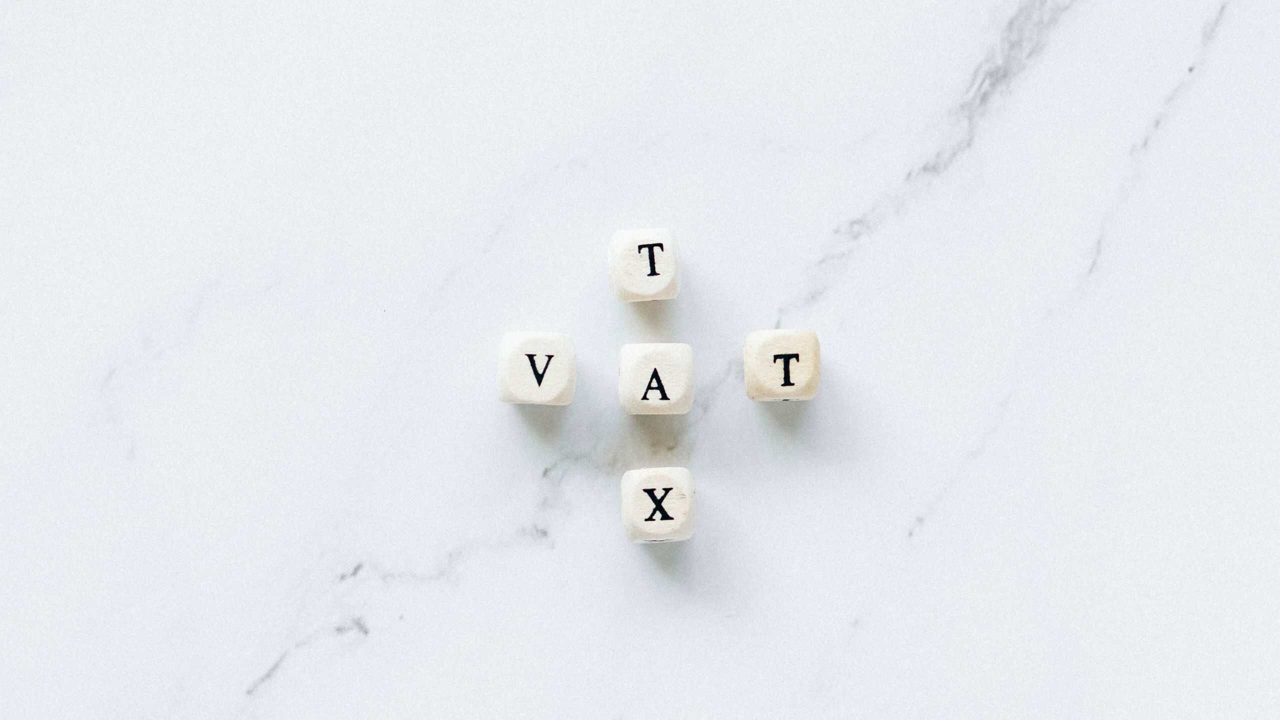 Wooden blocks spelling VAT on a white marble surface.