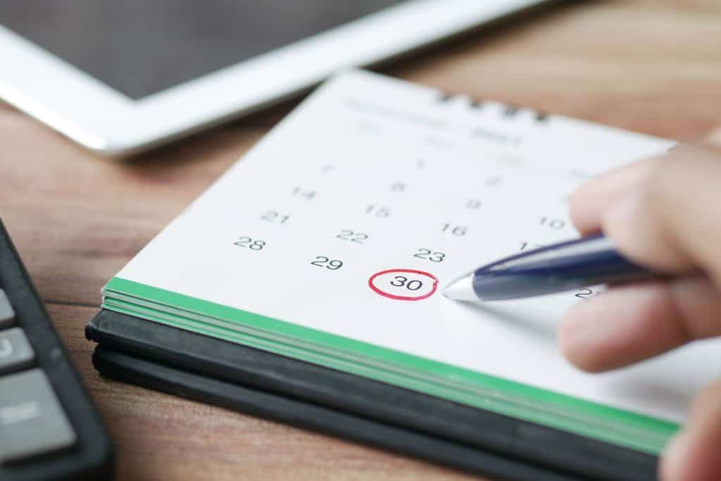 Person marking the 30th date on a calendar with a pen.