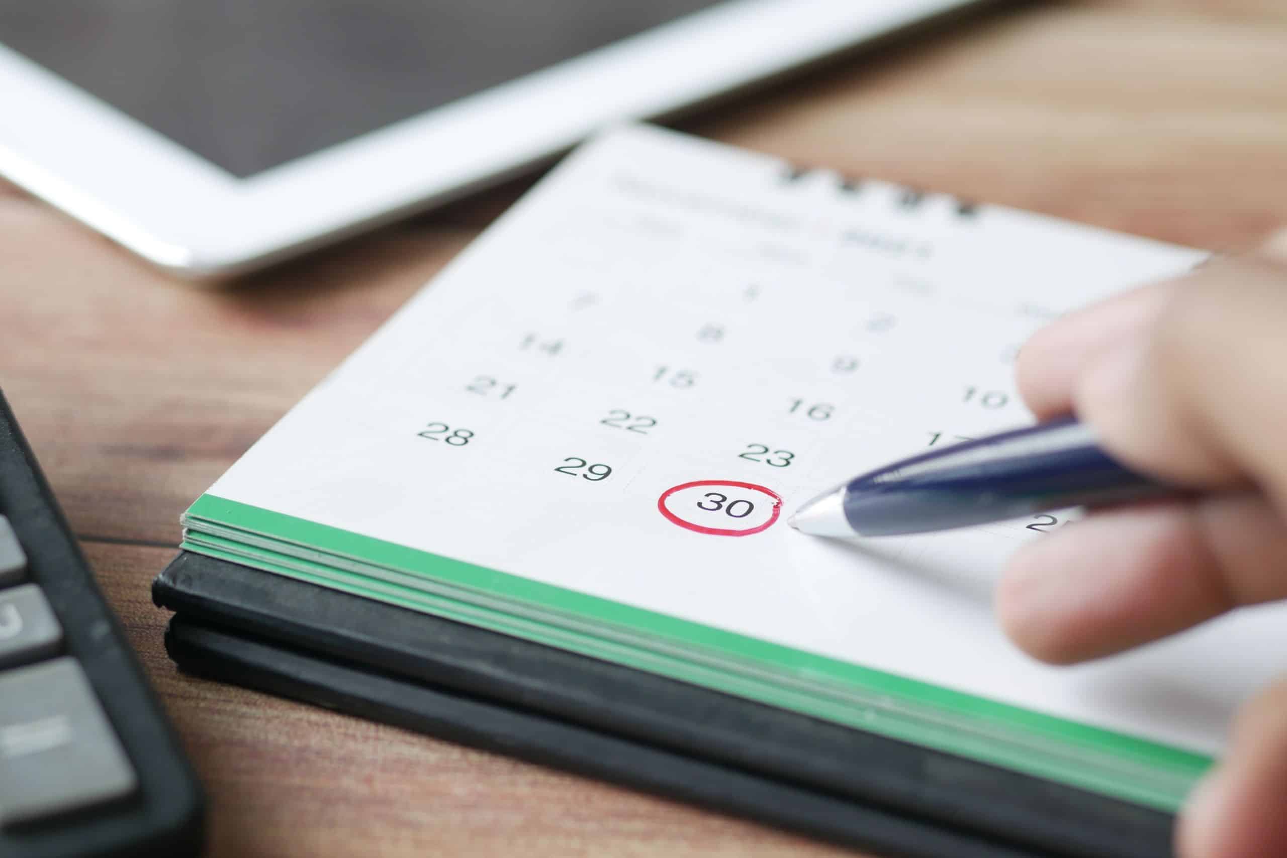 Person marking the 30th date on a calendar with a pen.